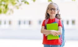 Kind mit Schulranzen vor der Schule